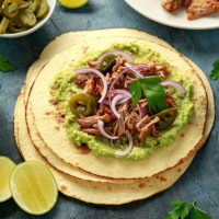 corn tortillas with pulled park on a slab with lime wedges
