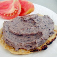 black bean spread on four-grain flatbread with tomato side on white plate