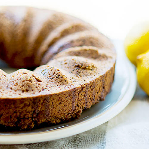 lemon spelt bundt cake on white plate with lemons in background