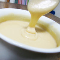 A large cup of vanilla cream frosting with a spoon taking a scoop out.