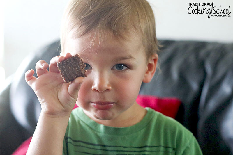 little blonde-haired boy looking into the camera and holding up half of a homemade Larabar