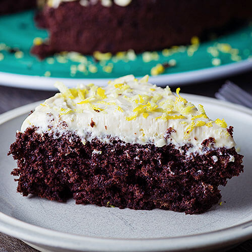 piece of chocolate torte with white frosting and lemon zest on blue plate