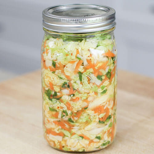 A quart mason jar with lid filled with kimchi sitting on a butcher block counter.