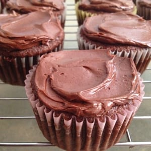 Chocolate cupcakes with chocolate coconut cream frosting sitting on a cooling rack.