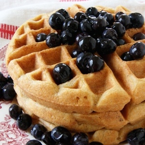 Sprouted flour coconut waffles stacked three high on a plate topped with blueberries.