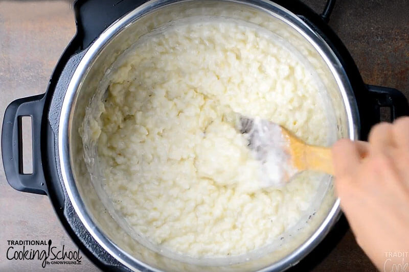 Instant pot filled with rice pudding and a wooden spoon stirring.