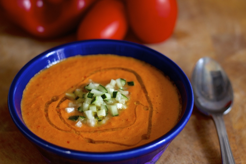 bright orange colored gazpacho garnished with oil and diced cucumber