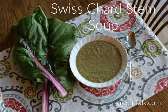 bowl of green colored soup on a table mat with a spoon and swiss chard nearby
