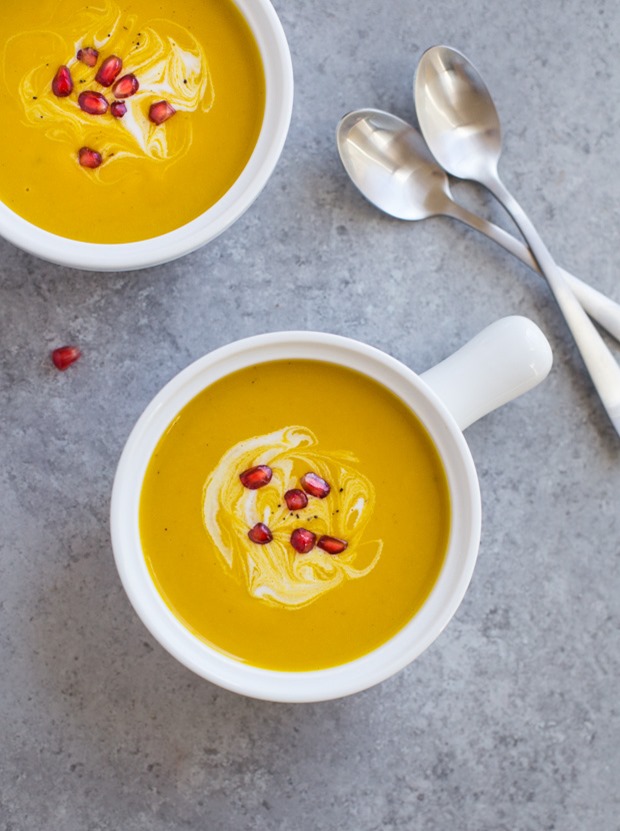 yellow soup in white bowls garnished with pomegranate arils