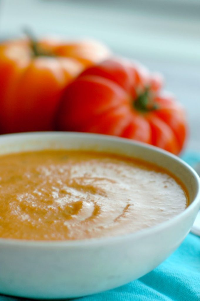 smooth orange blended soup in a bowl with fresh vibrant tomatoes in the background