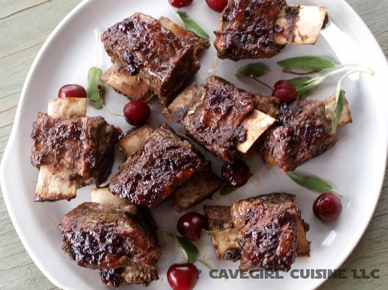 Cherry BBQ short ribs with a side of cherries and leaves on a white plate with black text overlay