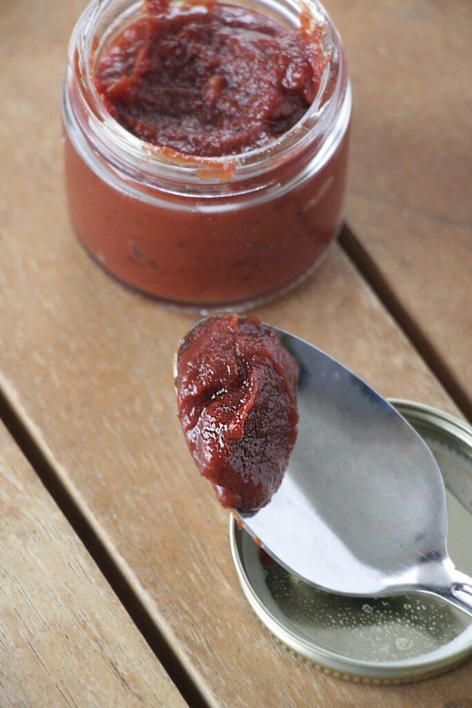 BBQ sauce in a jar with tasting spoon resting on the lid all on wooden table