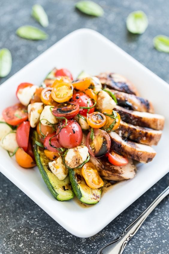 Balsamic grilled chicken with zucchini tomato caprice salad on white plate with fork