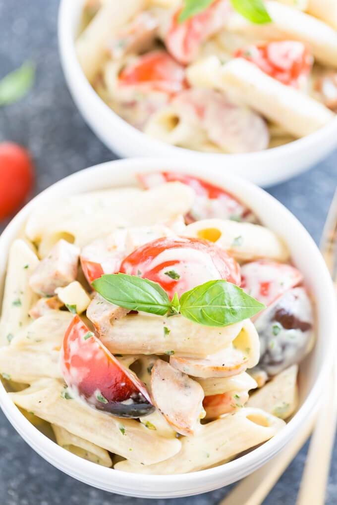 Pasta salad with basil and tomatoes in white bowl