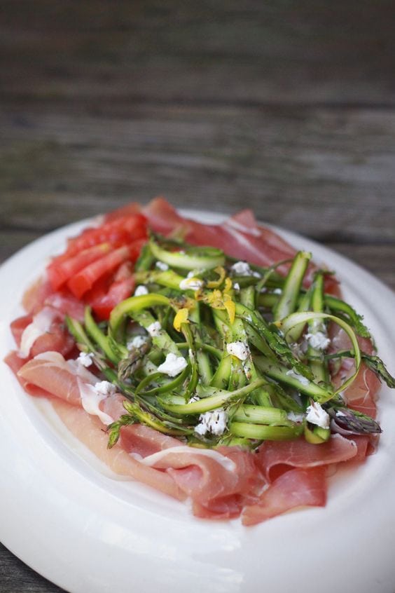 Asparagus salad on bed of prosciutto with side of tomatoes on a white plate