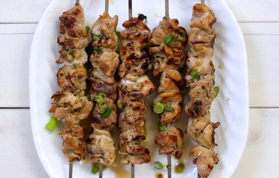 Chicken curry skewers with scallions on a white plate 