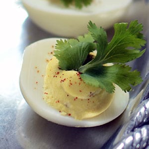 Fermented jalapeno deviled egg with a cilantro leaf on top sitting on a platter.