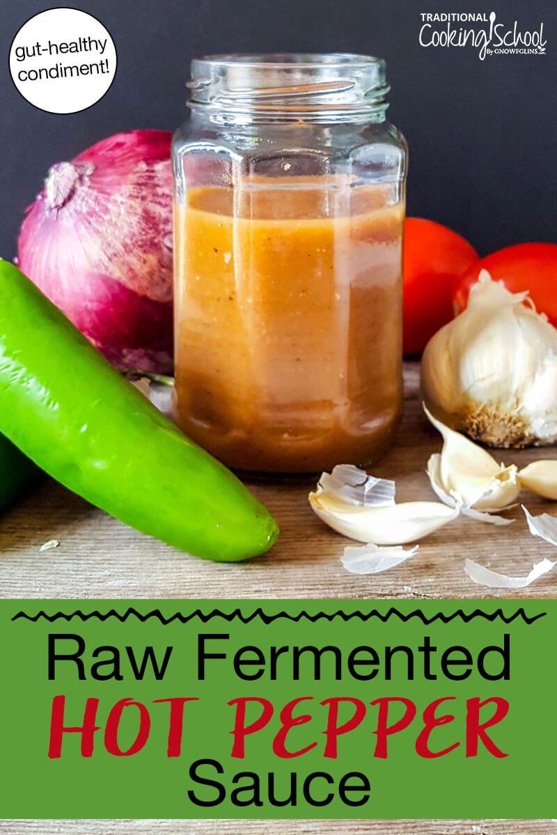 Homemade hot sauce in a small jar surrounded by tomatoes, garlic, onion, and a hot pepper. Text overlay says: "Raw Fermented Hot Pepper Sauce (gut-healthy condiment!)"