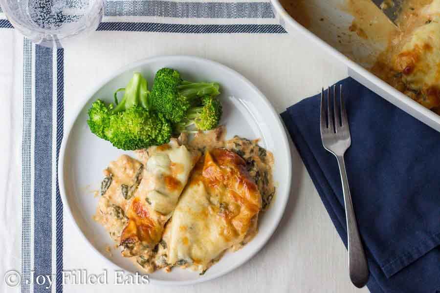 chicken smothered in cheese with broccoli on white plate with fork