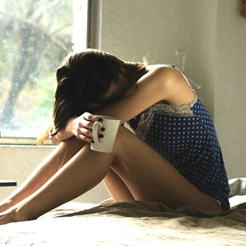 woman resting her head on her knees and holding a white mug