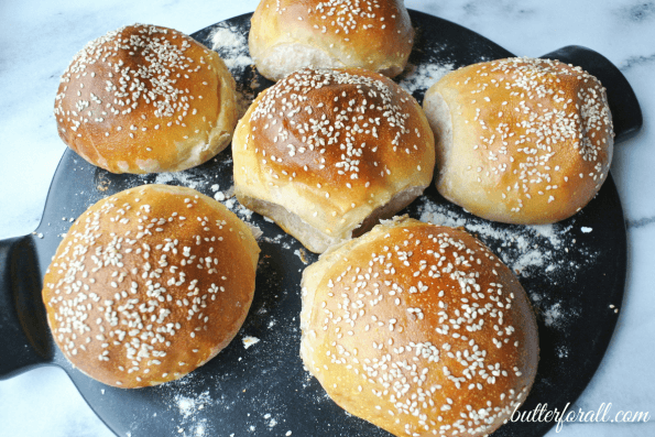 Soft chewy sourdough burger buns with sesame seeds on black pan