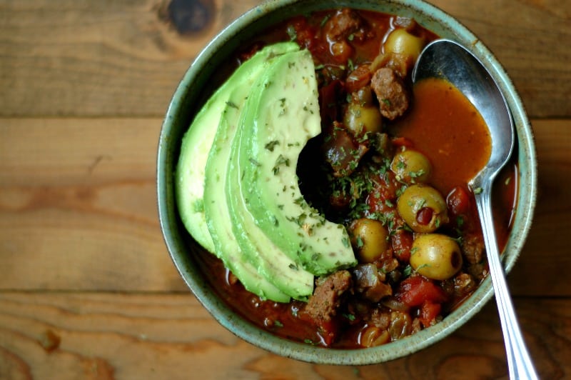 bowl of chili with avocado slices and green olives