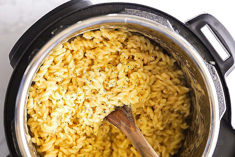 pressure cooker full of macaroni and cheese with a wooden spoon stirring it