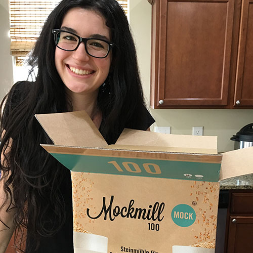 brunette smiles next to an open box with home stone grain mill inside