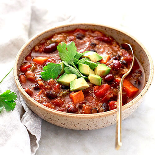 rustic bowl of chili with parsley and avocado garnishes and gold-colored spoon