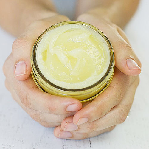 woman's hands cupped around a small glass jar of homemade salve