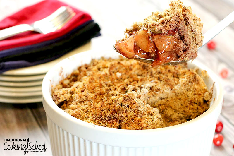 casserole dish of apple cranberry crisp with a spoon taking a scoop out of it