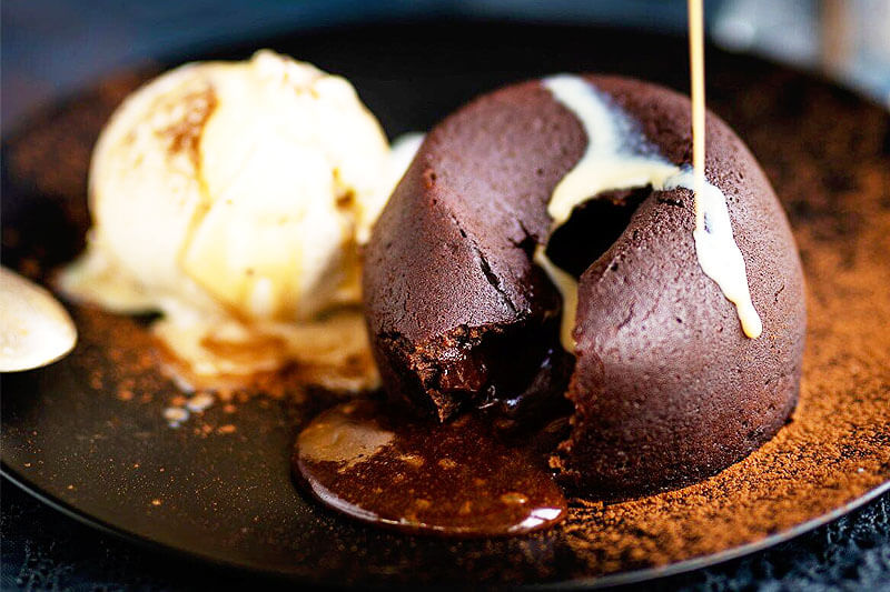 chocolate lava cake oozing chocolate with a drizzle of caramel sauce next to vanilla ice cream