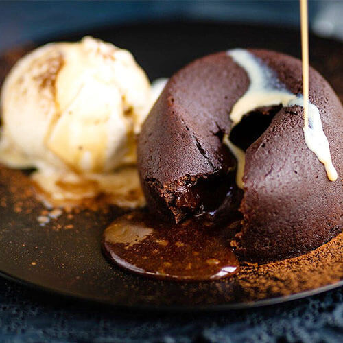 chocolate lava cake oozing chocolate with a drizzle of caramel sauce next to vanilla ice cream