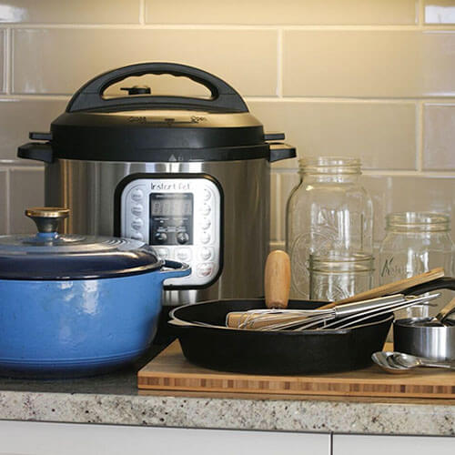 kitchen tools and appliances arranged on a counter, including an Instant Pot, Dutch oven, Mason jars, cast iron skillet, and utensils