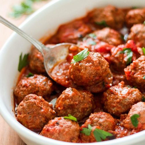 ceramic dish of saucy meatballs with spoon holding one