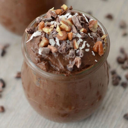 small glass cup of chocolate mousse garnished with chopped pecans, shredded coconut, and cacao nibs
