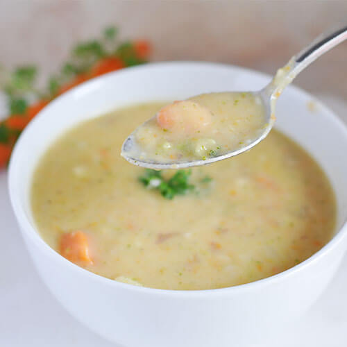 bowl of creamy veggie soup with a spoonful of it in focus and lifted to the foreground