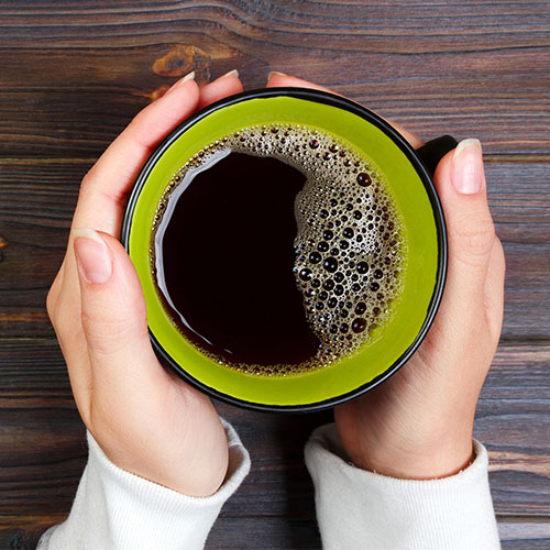 hands cupping a green mug of black coffee