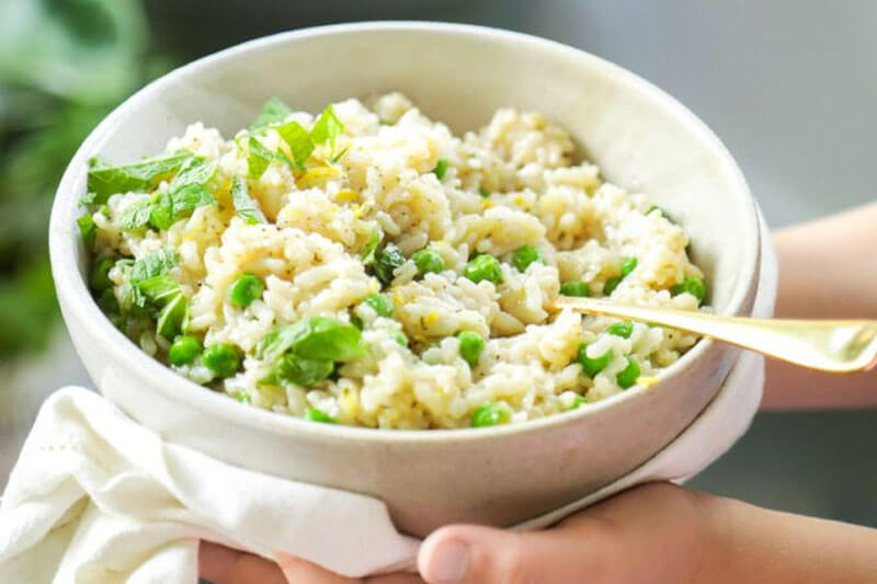 hands holding a bowl of spring-inspired risotto with fresh herbs and peas