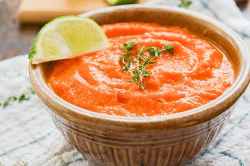 bowl of roasted carrot soup garnished with fresh herbs and a lime slice