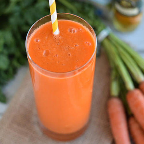 cup of bright orange carrot smoothie with a yellow and white striped straw