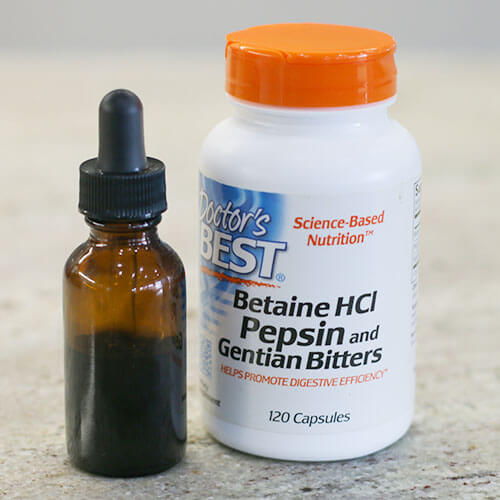 tincture in a small glass dropper bottle next to a white plastic bottle of Betain HCl Pepsin and Gentian Bitters on a counter