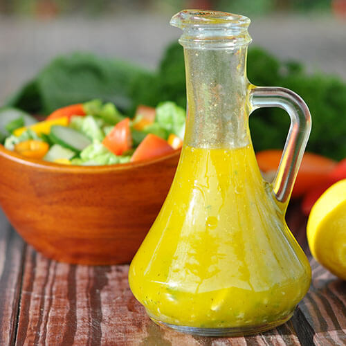 beautiful healthy salad dressing in front of a wooden bowl of salad