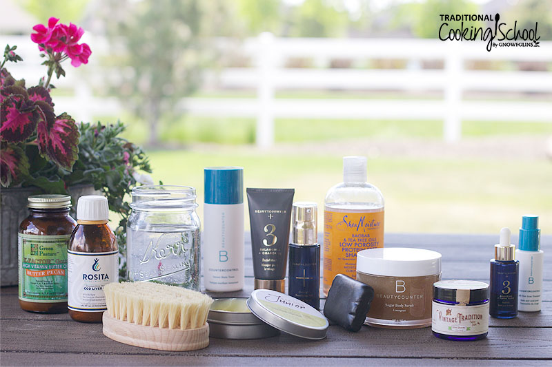 array of many different non-toxic products on a picnic table, including cod liver oil, tallow balm, Shea Moisture shampoo, BeautyCounter products, a dry brush, etc.