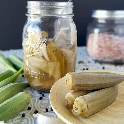 photo of how to make pickled okra recipe, with pint-sized Mason jar of already fermented okra, pickled okra on a plate, fresh okra, and sea salt