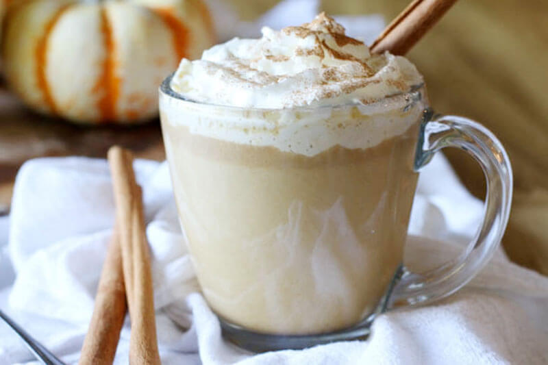 clear glass mug of a healthy pumpkin spice latte, with whipped cream on top and a cinnamon stick