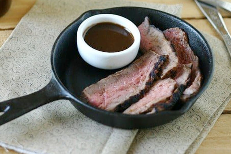 small cast iron skillet with a bowl of homemade copycat A1 steak sauce in it, next to strips of steak