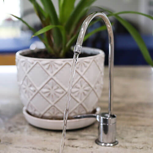 water faucet that is part of a whole house water filtration system, turned on so that it is clean water is flowing from it into the sink