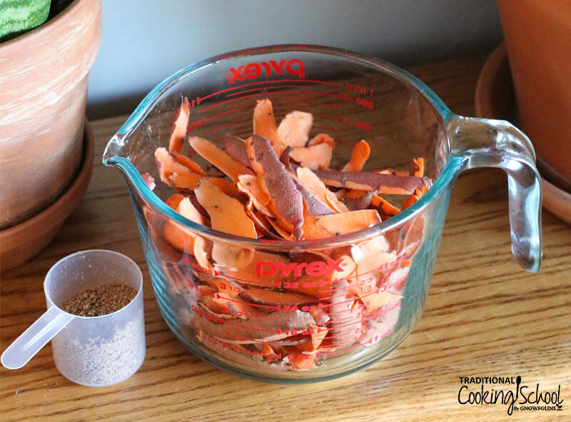 4-cup glass Pyrex measuring container full of sweet potato shavings next to a small plastic scoop of bokashi bran