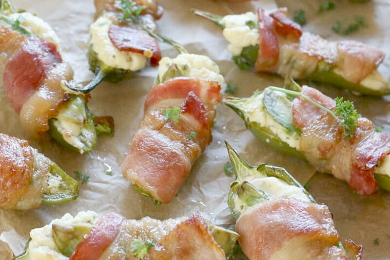 an array of bacon avocado jalapeno poppers on a sheet of parchment paper